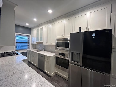 Kitchen with recessed lighting, glass insert cabinets, decorative backsplash, stainless steel appliances, and a sink