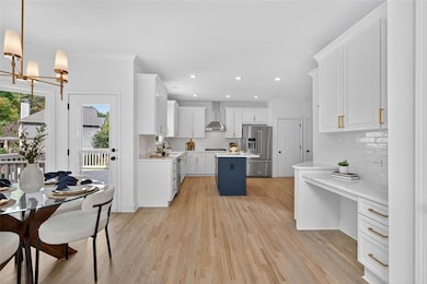 Kitchen with white cabinets, a kitchen island, light wood-style flooring, stainless steel appliances, and backsplash