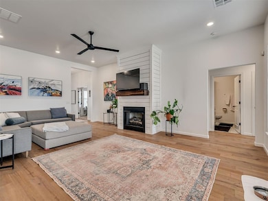 Living area featuring ceiling fan, a fireplace, light wood finished floors, recessed lighting, and baseboards