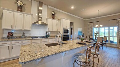 Kitchen featuring decorative backsplash, light wood-style flooring, wall chimney range hood, crown molding, and light stone counters