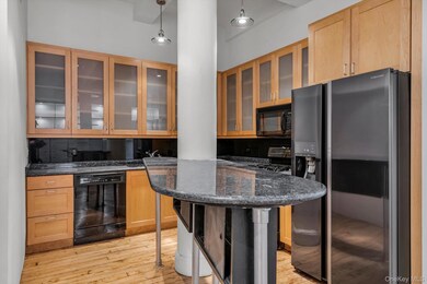 Kitchen with black appliances, hanging light fixtures, light wood-type flooring, dark stone counters, and light brown cabinetry