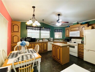 Kitchen featuring white appliances, ceiling fan with notable chandelier, hanging light fixtures, sink, and a kitchen island