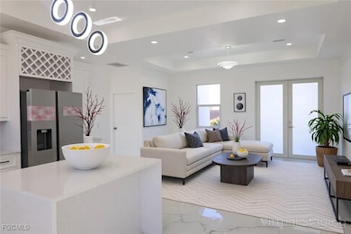 Living area featuring a tray ceiling, light marble finish floors, recessed lighting, and french doors