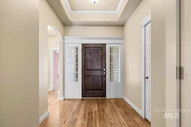Foyer entrance featuring light wood finished floors, a raised ceiling, and arched walkways
