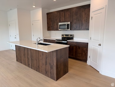 Kitchen with appliances with stainless steel finishes, dark brown cabinets, light wood finished floors, an island with sink, and recessed lighting