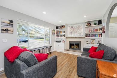Living room with a lit fireplace, light wood finished floors, recessed lighting, and arched walkways