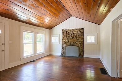Unfurnished living room with dark wood-style flooring, a stone fireplace, vaulted ceiling, wooden walls, and wood ceiling