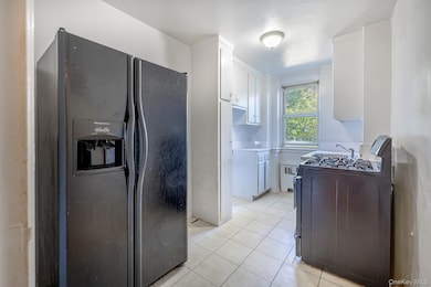 Kitchen featuring black refrigerator with ice dispenser, gas stove, light tile patterned flooring, white cabinetry, and light countertops