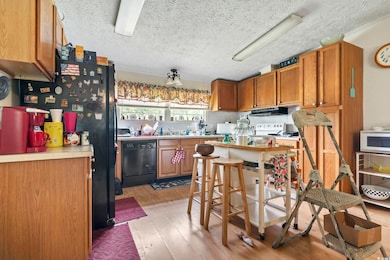 Kitchen with dishwasher, white microwave, under cabinet range hood, light wood-style floors, and brown cabinetry
