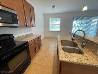 Kitchen with electric range, stainless steel microwave, pendant lighting, light tile patterned flooring, and light stone countertops