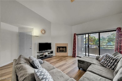 Living room with light wood finished floors, a tiled fireplace, and lofted ceiling