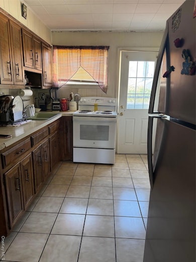 Kitchen with refrigerator, light tile patterned floors, white range with electric stovetop, and light countertops