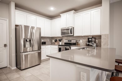 Kitchen featuring stainless steel appliances, backsplash, white cabinetry, sink, and a breakfast bar