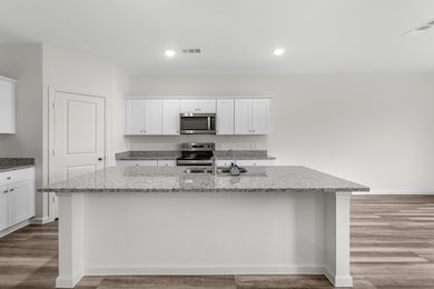 Kitchen with white cabinetry, light stone counters, dark wood-style flooring, appliances with stainless steel finishes, and recessed lighting
