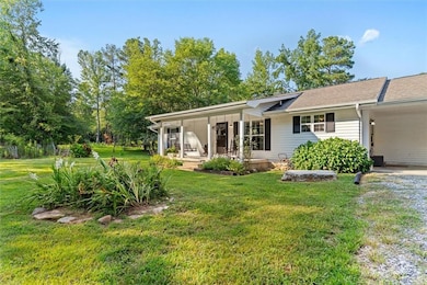 Rear view of property featuring a porch, a yard, an attached carport, and driveway