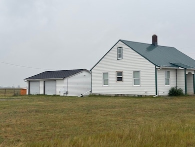 Rear view of property with a yard, a chimney, a detached garage, and a metal roof