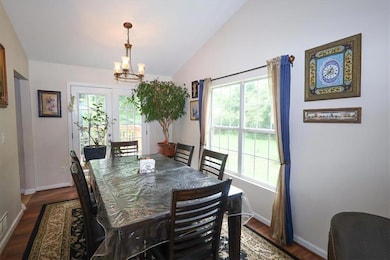 Dining space featuring a chandelier, plenty of natural light, vaulted ceiling, baseboards, and dark wood-style flooring