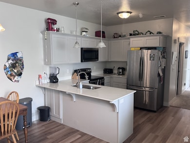 Kitchen featuring stainless steel appliances, a peninsula, a textured ceiling, dark wood-style flooring, and a breakfast bar