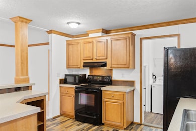 Kitchen featuring black appliances, under cabinet range hood, washer / dryer, ornate columns, and a textured ceiling