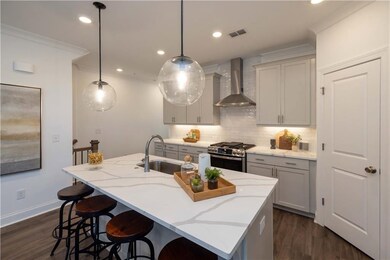 Kitchen with stainless steel gas stove, wall chimney exhaust hood, a sink, decorative backsplash, and a breakfast bar area