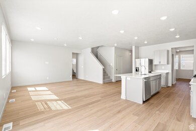 Kitchen featuring a center island with sink, appliances with stainless steel finishes, light wood-style floors, open floor plan, and recessed lighting