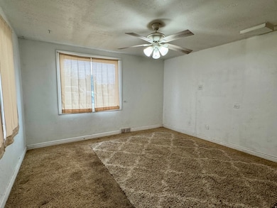 Empty room featuring a textured ceiling, carpet floors, and ceiling fan