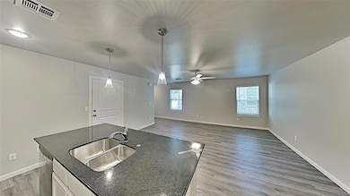 Kitchen with light wood-style flooring, a kitchen island with sink, ceiling fan, white cabinetry, and pendant lighting