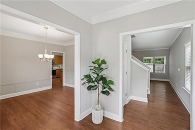 Corridor with a chandelier, dark wood-style floors, crown molding, and baseboards