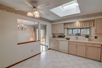 Kitchen with a skylight, sink, light tile floors, ceiling fan with notable chandelier, and white dishwasher