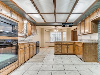 Kitchen with a peninsula, black appliances, brown cabinetry, and light tile patterned floors