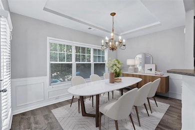 Dining area featuring a tray ceiling, a wainscoted wall, dark wood-type flooring, a chandelier, and a decorative wall