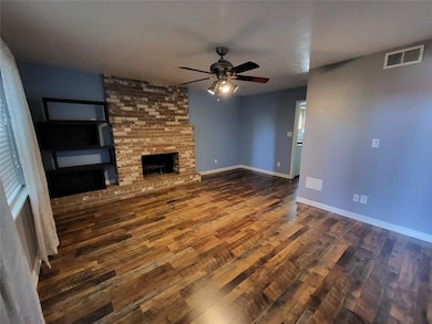 Unfurnished living room featuring dark wood-type flooring, a brick fireplace, and a ceiling fan