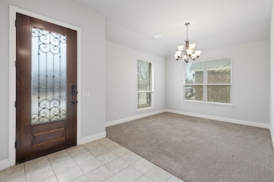 Foyer with baseboards, an inviting chandelier, light tile patterned floors, and light carpet