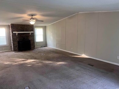 Unfurnished living room with crown molding, ceiling fan, carpet flooring, a stone fireplace, and a textured ceiling