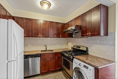 Kitchen featuring washer / clothes dryer, stainless steel appliances, exhaust hood, and decorative backsplash