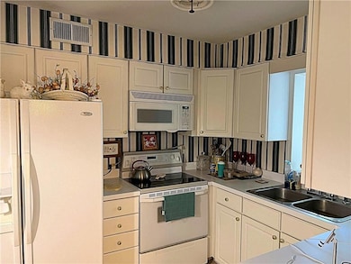Kitchen featuring wallpapered walls, white appliances, light countertops, and white cabinets