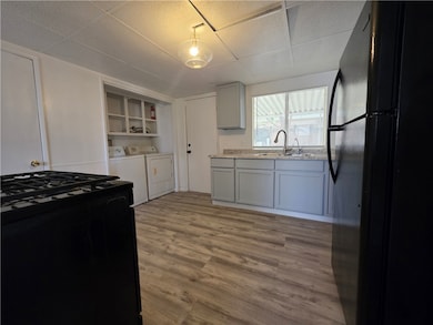 Kitchen featuring black appliances, washing machine and clothes dryer, dark wood-style flooring, gray cabinetry, and a drop ceiling