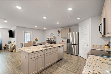 Kitchen with appliances with stainless steel finishes, a sink, light wood-type flooring, a kitchen island with sink, and recessed lighting