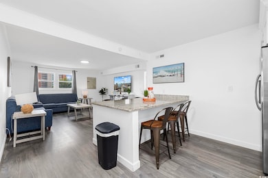 Kitchen featuring dark wood-type flooring, light stone countertops, a peninsula, and a breakfast bar area