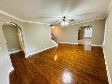 Empty room with ceiling fan, wood finished floors, ornamental molding, arched walkways, and baseboards