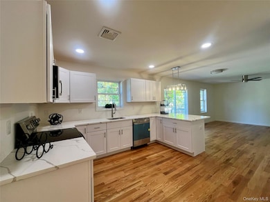 Kitchen with white cabinets, stainless steel appliances, light stone countertops, a peninsula, and light wood finished floors