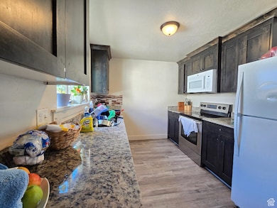 Kitchen featuring white appliances, light stone countertops, light wood-style floors, and a textured ceiling