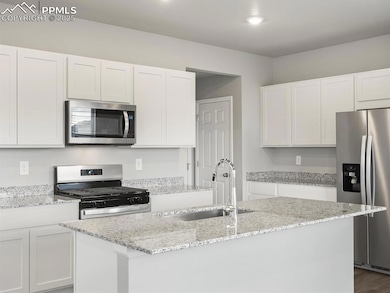 Kitchen featuring stainless steel appliances, white cabinets, light stone counters, and recessed lighting