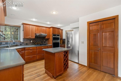 Kitchen with appliances with stainless steel finishes, under cabinet range hood, light wood-type flooring, backsplash, and brown cabinetry