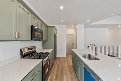 Kitchen featuring stainless steel range with gas cooktop, light stone countertops, green cabinets, light wood-style flooring, and recessed lighting