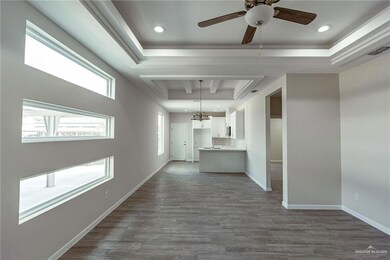 Unfurnished living room with ceiling fan with notable chandelier, light hardwood / wood-style floors, and a tray ceiling