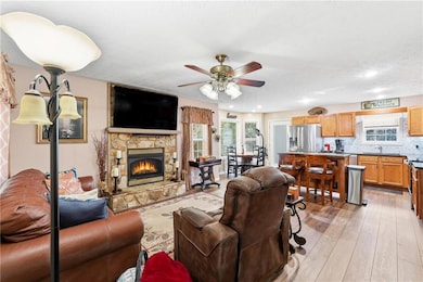 Living area featuring plenty of natural light, light wood-style floors, a stone fireplace, a ceiling fan, and a textured ceiling