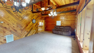 Unfurnished living room featuring a chandelier, carpet flooring, wood walls, and wood ceiling
