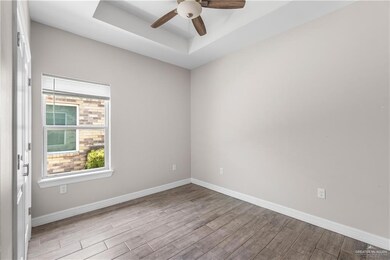 Empty room with wood finished floors, a raised ceiling, a ceiling fan, and baseboards