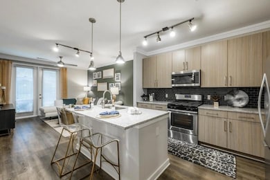 Kitchen with ceiling fan, stainless steel appliances, an island with sink, light stone counters, and track lighting